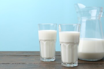 Fresh milk on wooden table against light blue background