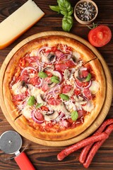 Tasty pizza with smoked sausages, ingredients and cutter on wooden table, flat lay