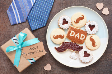 Fathers Day table scene. Overhead view on a dark stone background. Plate of chocolate mustache, heart and dad cookies with gift box, ties and Happy Father's Day greeting card.