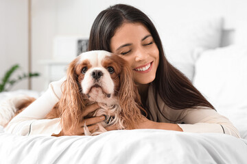 Beautiful young woman with cute cavalier King Charles spaniel lying on bed at home