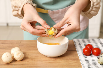 Woman breaking quail egg into bowl at wooden table, closeup
