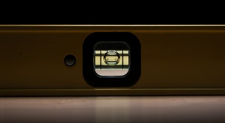 A close-up macro shot of a yellow spirit level, with the bubble centered in the vial, indicating a perfectly horizontal surface, resting on a wooden table against a dark background.