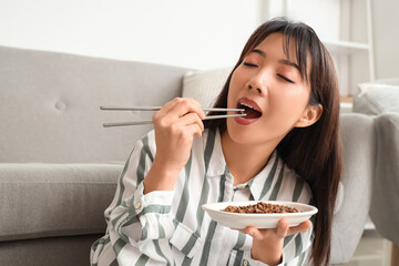 Beautiful Asian woman with chopsticks eating fried insects at home, closeup