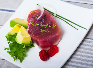 Tasty pan seared tuna (tataki) served on white plate with avocado, sun-dried tomatoes and greens