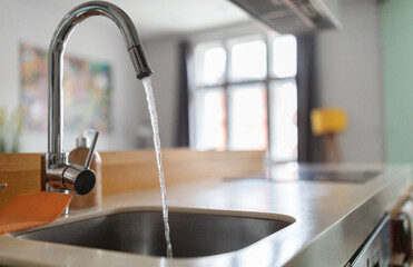 Close up shot of modern kitchen faucet with water running from tap, flow falling to empty dish sink...