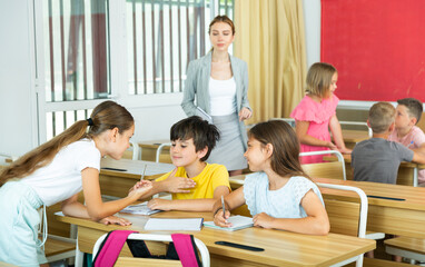 Group of diligent school kids discussing something in group during lesson in classroom in...