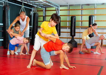 Boys and girls in gym exercising armlock move during group self-defence training.