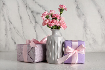 Vase with beautiful carnation flowers and gift boxes on white background. Mother's Day celebration