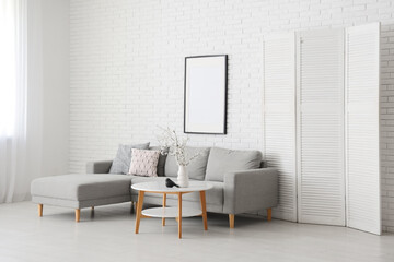 Interior of stylish living room with grey sofa, folding screen and blooming tree branches on coffee table