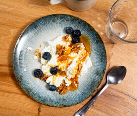 On white plate, portion of grainy cottage cheese sweetened with transparent yellow honey, completed...