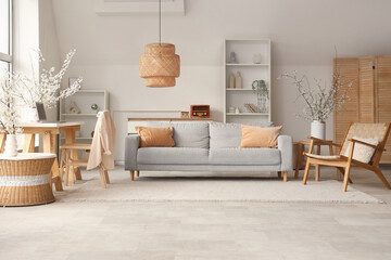 Interior of light living room with sofa, workplace and blossoming branches in vases