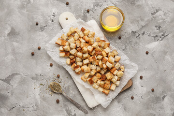 Cutting board with crunchy croutons, peppercorns and glass bowl of oil on grey background