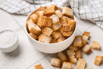 Bowl with crunchy croutons and salt on white tile background, closeup