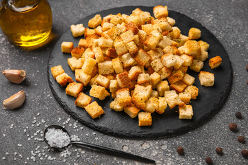Black board with crunchy croutons and different spices on dark background, closeup