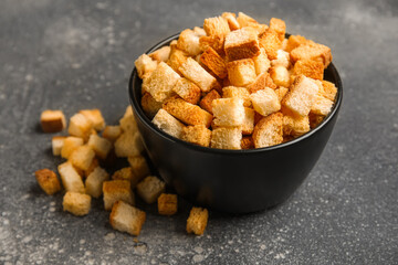 Bowl with crunchy croutons on dark background, closeup