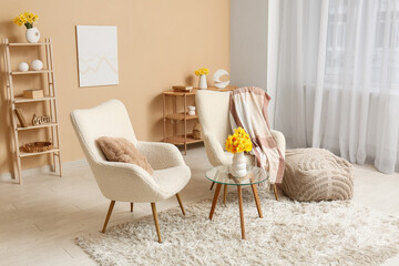 Cozy armchairs with shelving units, coffee table and narcissus flowers against beige wall in living room