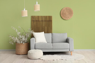 Interior of living room with sofa, folding screen and beautiful blooming branches in wicker vase