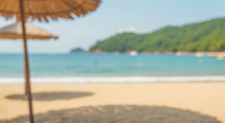 Fototapeta premium Blurred tropical beach scene with straw umbrella, golden sand, and turquoise sea. Summer vacation concept. Defocused background for relaxation and travel advertisement.