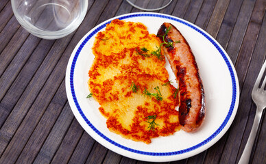 Portion of potato pancakes with roasted sausage served on plate.