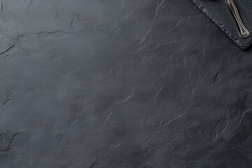 Dark gray stone surface with utensils.  Top view of a textured black slate table top with a few utensils, creating a minimalist and modern background
