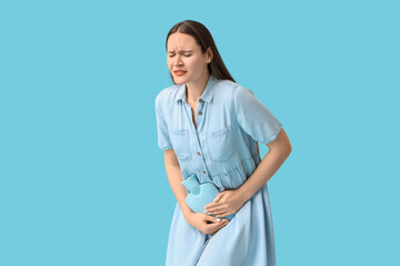 Young woman with hot water bag on blue background. Cystitis concept