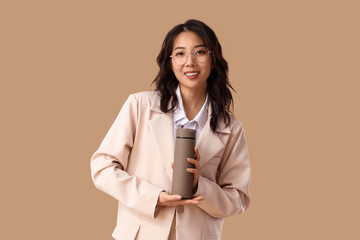 Young Asian businesswoman with thermos on beige background