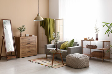 Sofa with folding screen, dressers and vases of white blooming branches near window in living room