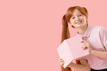 Cute redhead schoolgirl with book on pink background