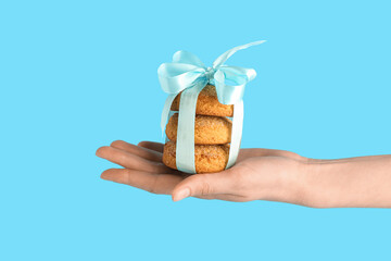 Female hand holding sweet cookies tied with ribbon on blue background