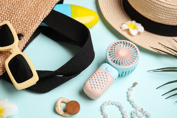 Bag with female summer accessories and mini fan on blue background
