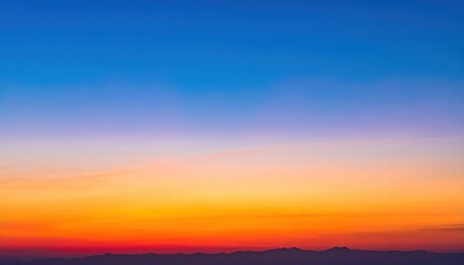Obraz premium A stunning sunset painting the sky in vibrant hues of orange, pink, and blue, with silhouettes of distant mountains on the horizon