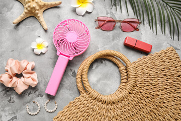 Bag with female summer accessories and mini fan on grunge background