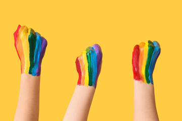 Female hands with painted fists in colors of LGBT flag on yellow background