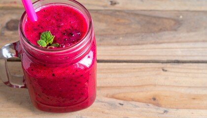 Vibrant red dragon fruit smoothie in mason jar with fresh fruit garnish and condensation on rustic wood table isolated background
