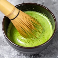 Vibrant matcha tea being whisked into frothy perfection in a rustic raku tea bowl with bamboo chasen.