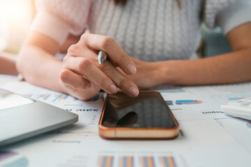 A person interacts with a smartphone and pen on a desk filled with business documents and a laptop, bathed in sunlight.