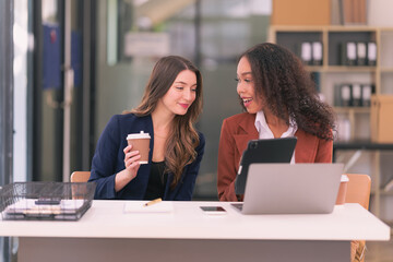 Two businesswomen in suits working and brainstorming together using computer technology documents financial graphs for analysis in modern office