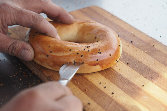 Preparing a fresh bagel with sesame seeds on a wooden cutting board