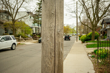 Wooden utility pole with staples from posted handbills center of frame out of focus residential street scene in background room for text	
