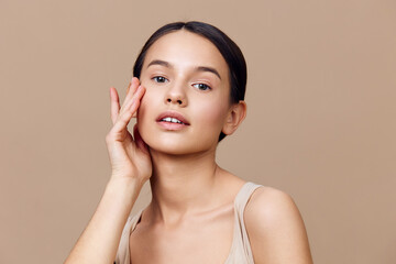 Portrait of a young woman with natural makeup and a serene expression against a warm beige...