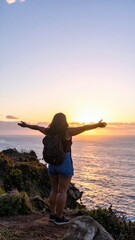 Fototapeta premium Traveler Standing on Cliff Overlooking Ocean at Sunrise with Arms Wide Open Embracing Freedom and Spirit of Exploration
