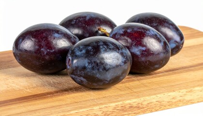 Obraz premium Oval-shaped safou fruits with glossy blue-purple skin and buttery flesh on wooden chopping board isolated background, full depth of field