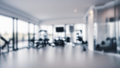 Blurred gym interior with large windows and exercise equipment in a bright space.
