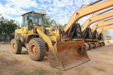 Lots of excavators parked on construction area of industrial building in construction site under the blue sky background.Earthmoving construction equipment