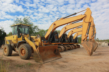 Lots of excavators parked on construction area of industrial building in construction site under the blue sky background.Earthmoving construction equipment