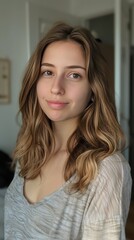 Fototapeta premium Portrait of a young woman with wavy hair, natural makeup, and a serene expression indoors.