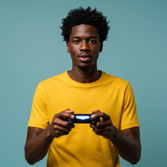 Young Black man in a yellow t-shirt holding a video game controller in front of a teal background. Focused gaze, casual pose, and centered against a studio backdrop.