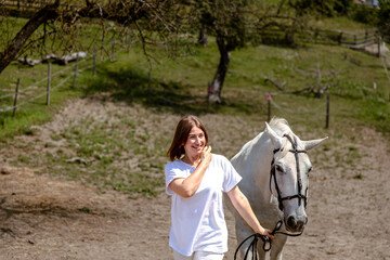 Young caucasian female leading white horse outdoors on sunny day