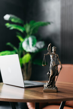 Lawyer's office. Statue of justice with scales and a laptop in a modern office cubicle. Concept of legal law, counseling and concept of justice.
