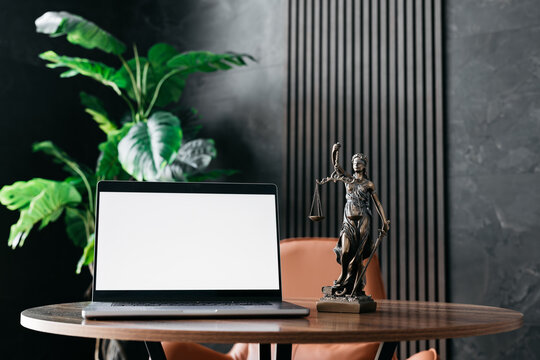 Lawyer's office. Statue of justice with scales and a white screen laptop in a modern office cubicle. Layout for advertising. Concept of legal law.